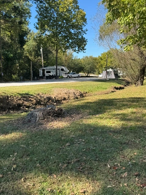 A camper parked in a wooded clearing with a dry ditch in the foreground.