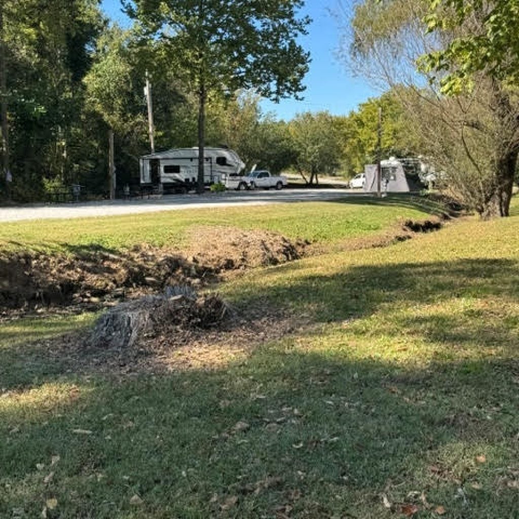 A camper parked in a wooded clearing with a dry ditch in the foreground.