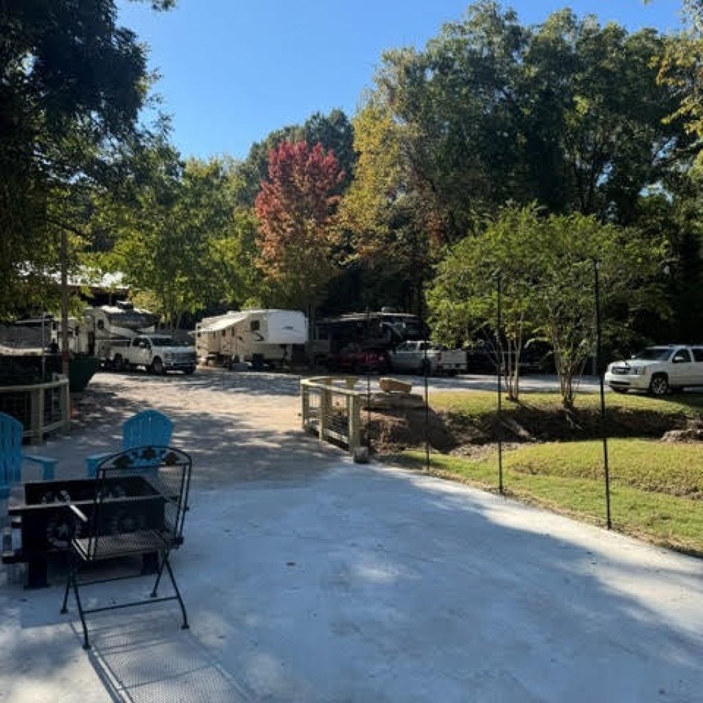 An outdoor patio area overlooking a paved parking lot with several recreational vehicles and cars parked among trees.