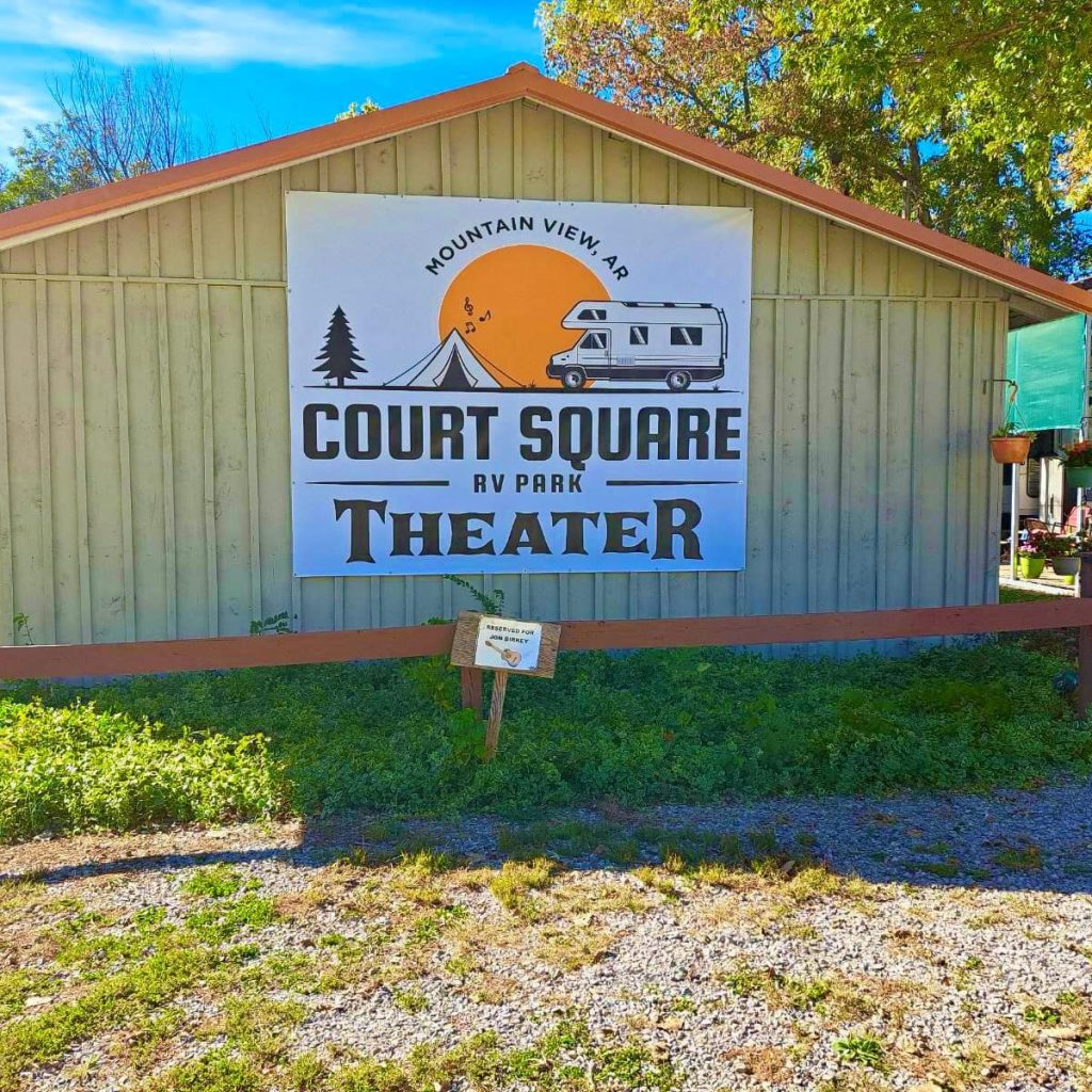 Sign for Court Square RV Park Theater, Mountain View, AR, on a wooden building with trees and greenery around.